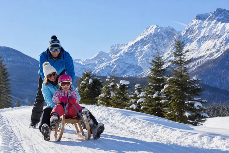 Family sledging in front of snowy mountains at a ski resort